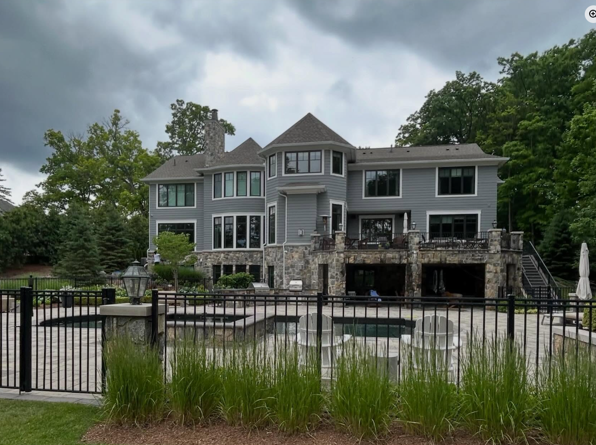 Rear lakefront view of a Bloomfield Hills shingle-style home with bay windows and turret cleaned by Apex Exteriors